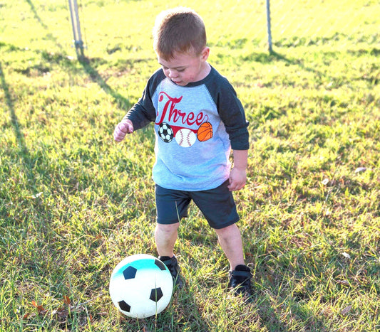 Three Design on a Raglan (Baseball Style) shirt with a soccer, baseball and basketball on the front under the Three.
